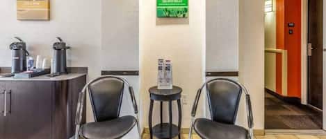 A reception area with a counter, two chairs, a small table, and a poster on the wall.