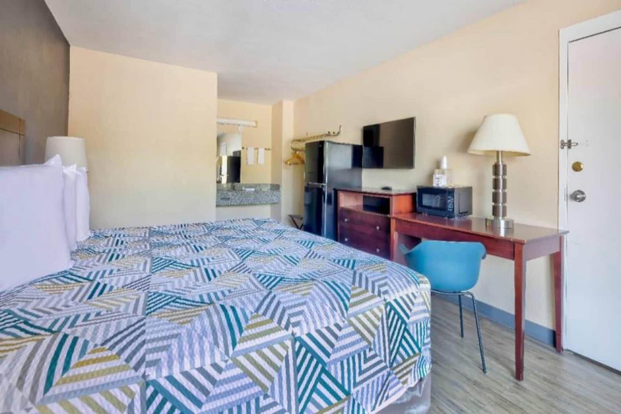 Una habitación de hotel con cama, escritorio, silla, televisor y puerta.