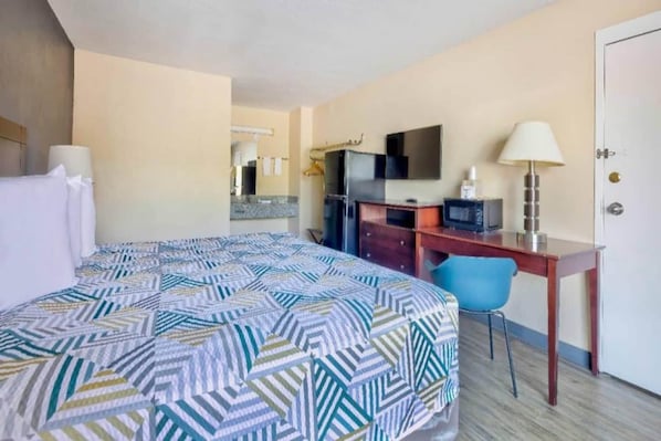 A hotel room with a bed, a desk, a chair, a television, and a door.