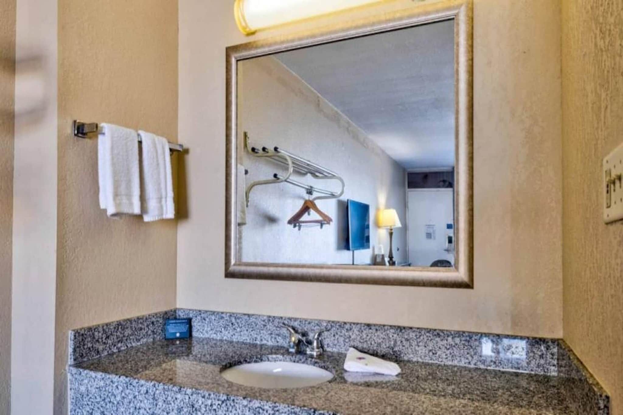 A hotel bathroom with a granite countertop, a sink, a mirror, and a towel rack.