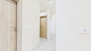 A hallway with a wooden door, a light switch, and a tiled floor. - New Suite 3-bedroom Apartment With Sea View (Umag)
