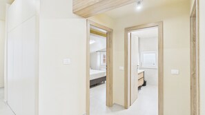 Un couloir menant à une chambre à coucher, qui contient un lit, une table de chevet et une fenêtre.