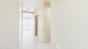 Ein Flur mit einer Tür, die auf einen Balkon führt, einem Lichtschalter an der Wand und einer Steckdose am Boden.