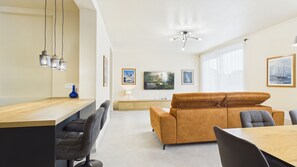 Un salon moderne avec un canapé, une table à manger et des chaises. Il y a un téléviseur accroché au mur et une fenêtre avec des rideaux.