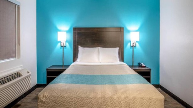 Quarto de hotel com cama, duas mesinhas de cabeceira, aquecedor fixado na parede e duas luminárias de parede.