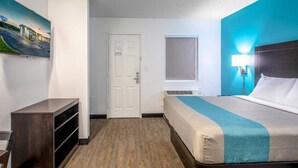 A hotel room with a bed, a desk, a chair, a window, and a painting on the wall. - 1 Queen Bed|Micfridge,Non-Smoking (Greenville)