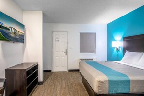 Habitación de hotel con cama, escritorio, silla, ventana y un cuadro en la pared.