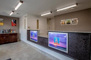 Zona de recepción con mostrador, máquina de café y una pantalla de televisión en la pared mostrando un canal de viajes.