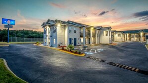 Um motel com estacionamento, uma placa indicando o número 6 e um pôr do sol ao fundo.