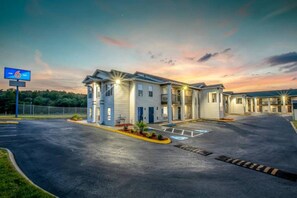 A motel with a parking lot, a sign indicating the number 6, and a sunset in the background. - 1 Queen Bed|Premium,Kitchen,Smk (Greenville)