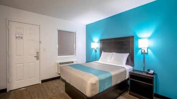 Quarto de hotel com cama, mesas de cabeceira, janela e porta.