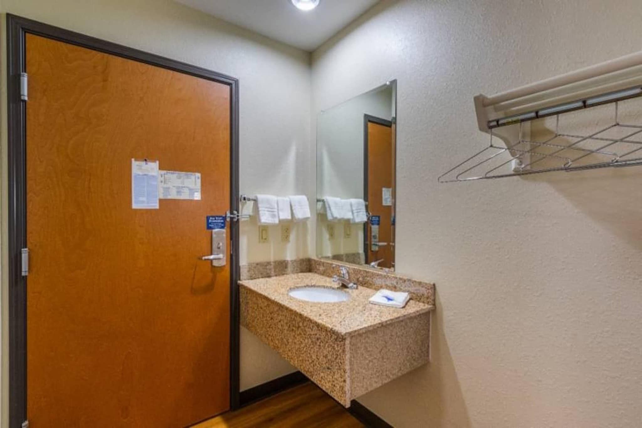 A hotel bathroom with a wooden door, a sink with a mirror, and a towel rack.