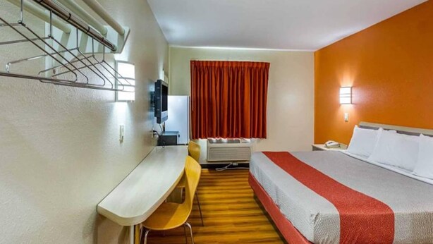 Habitación de hotel con cama, escritorio, silla, equipo de aire acondicionado y ventana con cortinas.