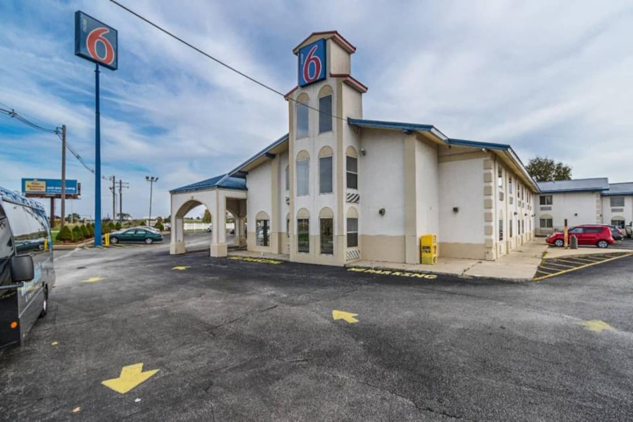 Un motel con un llamativo letrero con el número '6', una zona de estacionamiento techada y un cielo despejado.