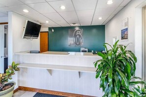 A reception desk with a digital screen, a number '6' sign, and a potted plant.