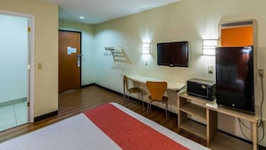 Una habitación de hotel con una cama, un escritorio con una silla, un televisor y un microondas.