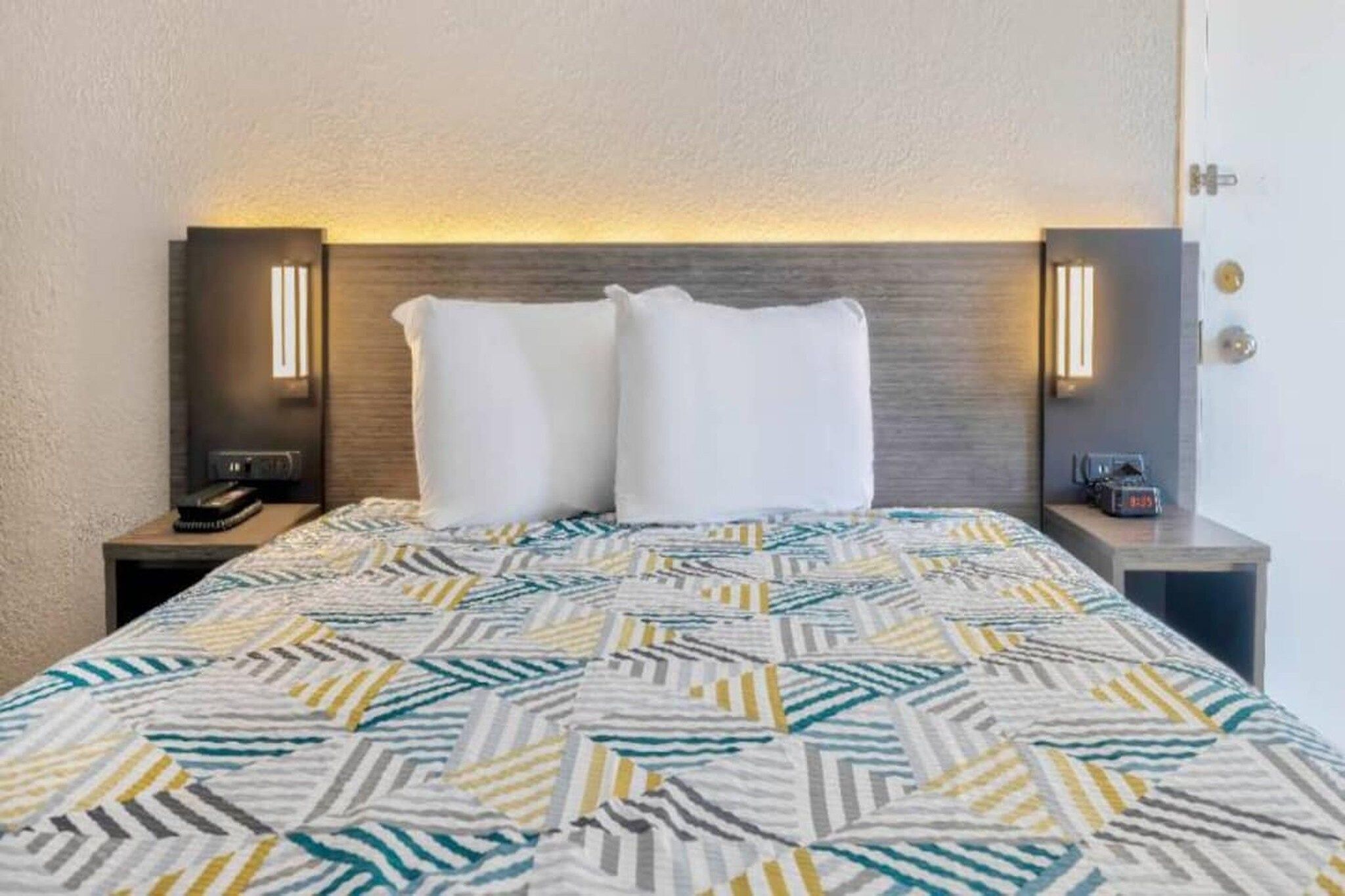 Une chambre d’hôtel comprenant un lit, deux tables de chevet, une petite table et une lampe fixée au mur.