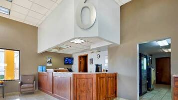 Una zona de recepción con mostrador de madera, un reloj y un televisor en la pared.