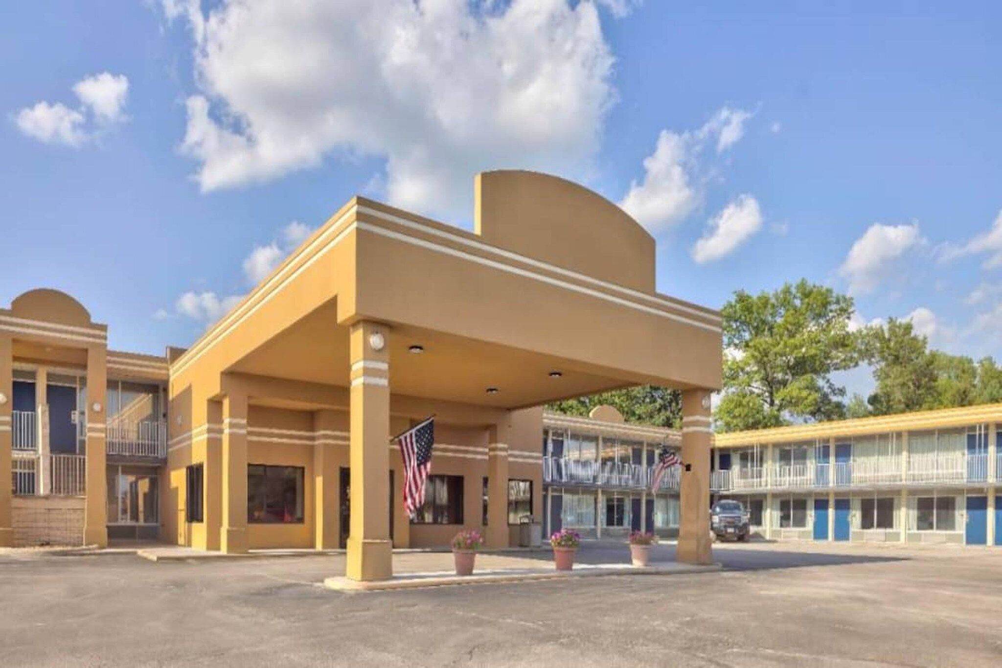 A hotel with a covered entrance, American flags, and a parking lot.