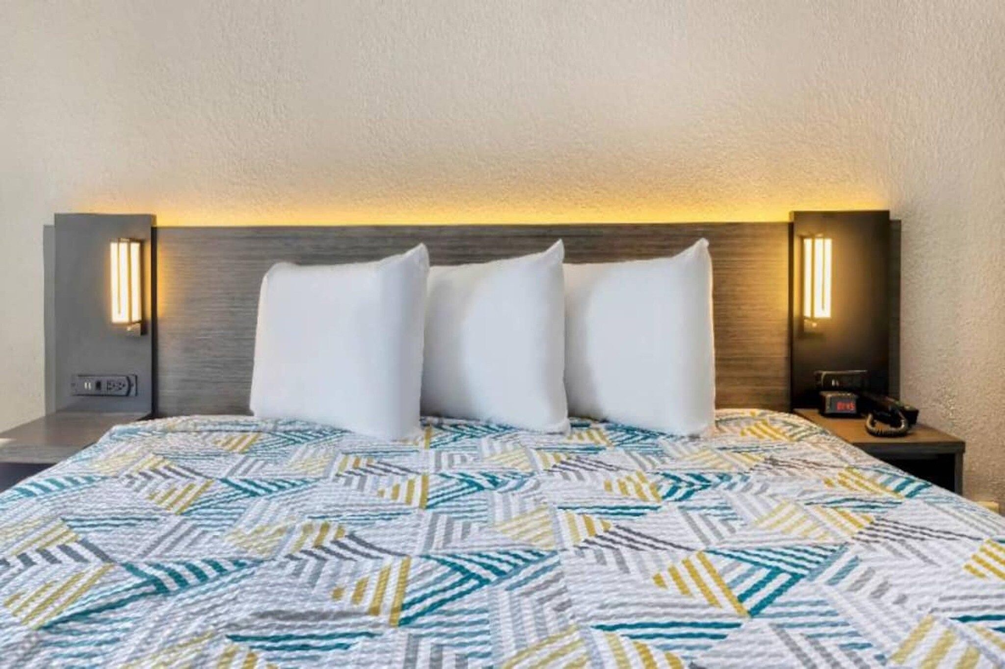 Ein Hotelzimmer mit einem Bett, zwei Nachttischen und einem Kopfteil mit integrierter Beleuchtung.