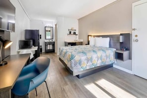 Une chambre d’hôtel moderne équipée d’un lit, d’un bureau, d’une chaise et d’une petite kitchenette.