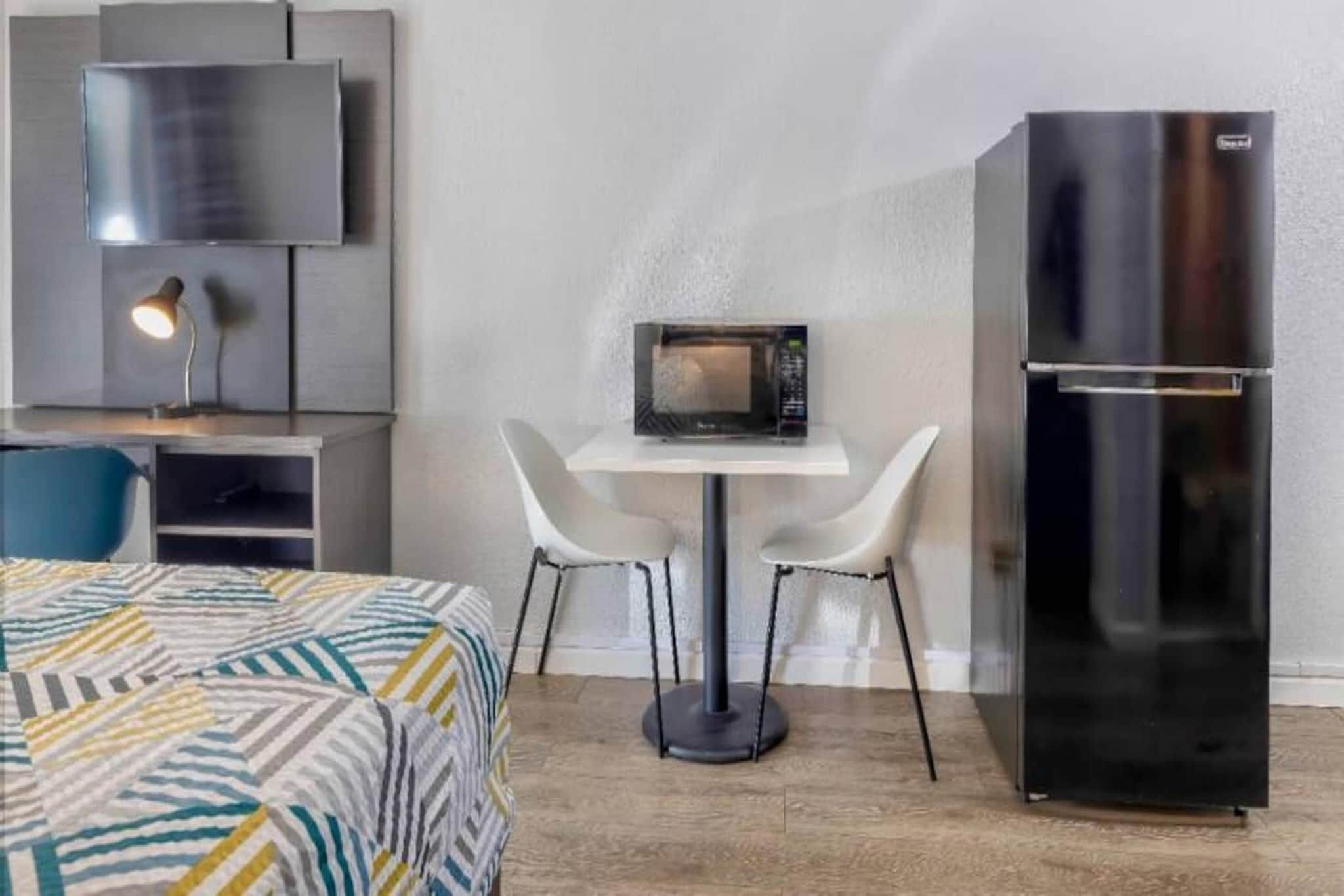 Une chambre d’hôtel compacte comprenant un lit, une petite table avec deux chaises, un four à micro-ondes, un réfrigérateur et un téléviseur fixé au mur.
