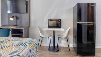 Une chambre d’hôtel compacte comprenant un lit, une petite table avec deux chaises, un four à micro-ondes, un réfrigérateur et un téléviseur fixé au mur.