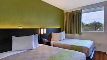Habitació d'hotel amb dos llits, una taula de nit, una làmpada i una finestra amb cortines.