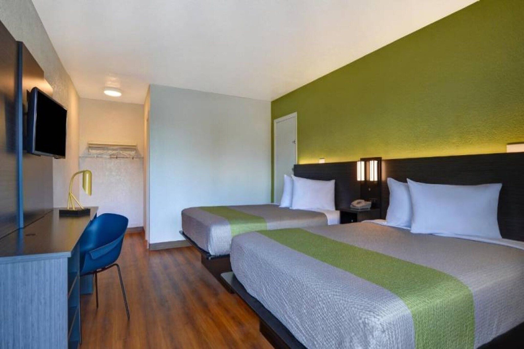 A hotel room with two beds, a desk, a chair, and a television.