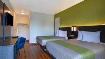 A hotel room with two beds, a desk, a chair, and a television.