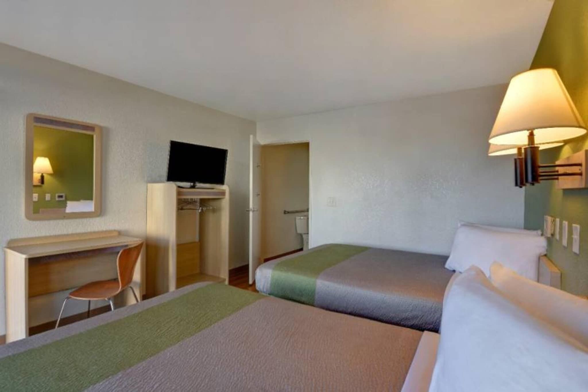 Een hotelkamer met een bureau, twee bedden, een televisie en een badkamer.