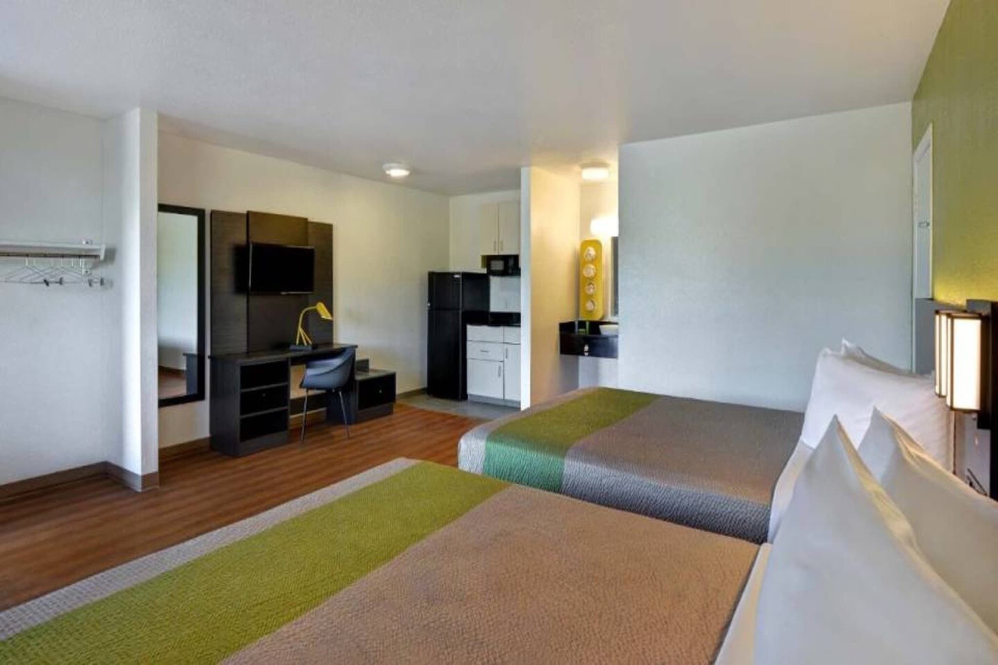 A hotel room with two beds, a desk, a chair, a TV, a wardrobe, and a bathroom.