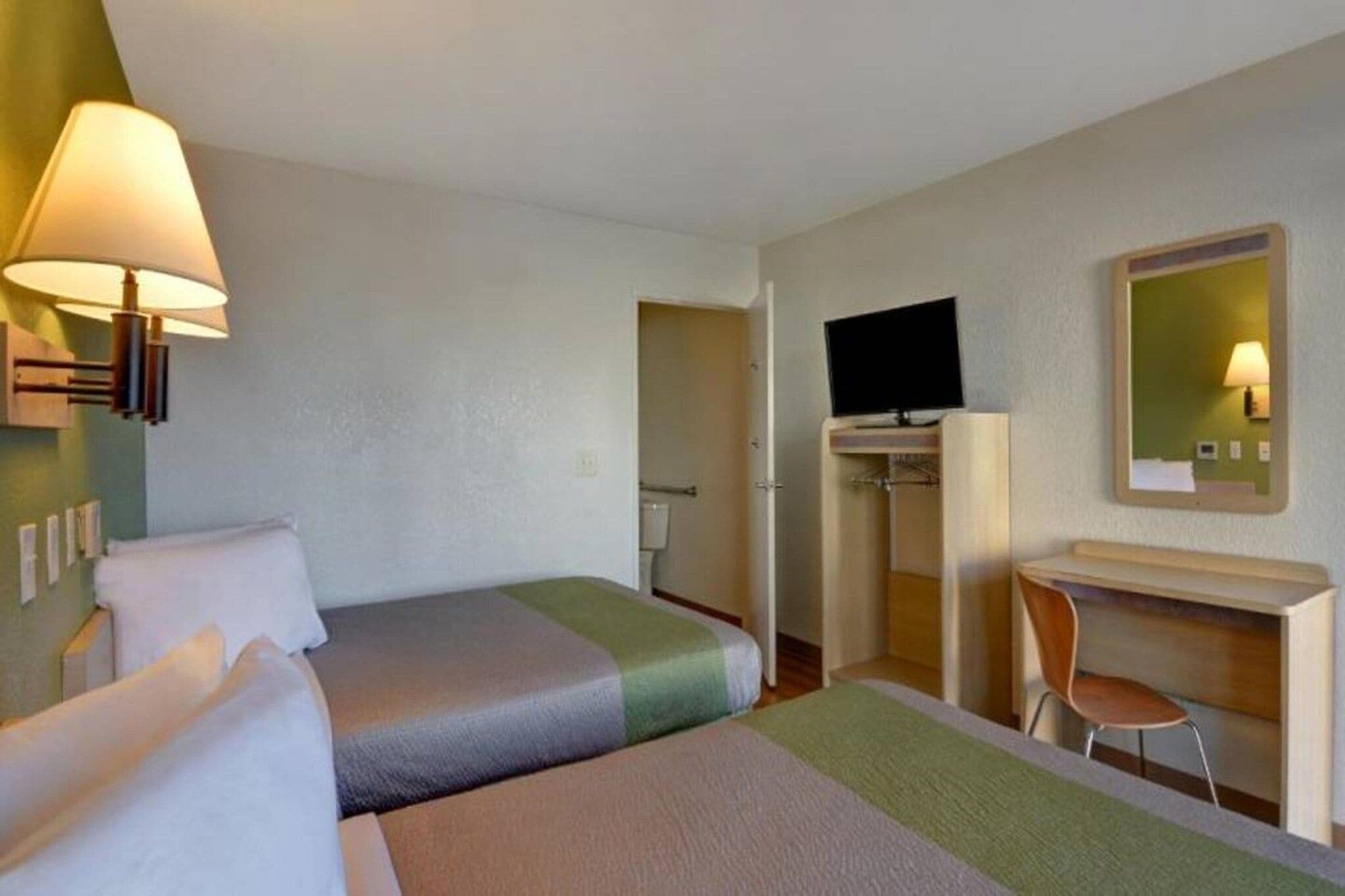 Habitación de hotel con dos camas, un escritorio, una silla, un televisor y un espejo.