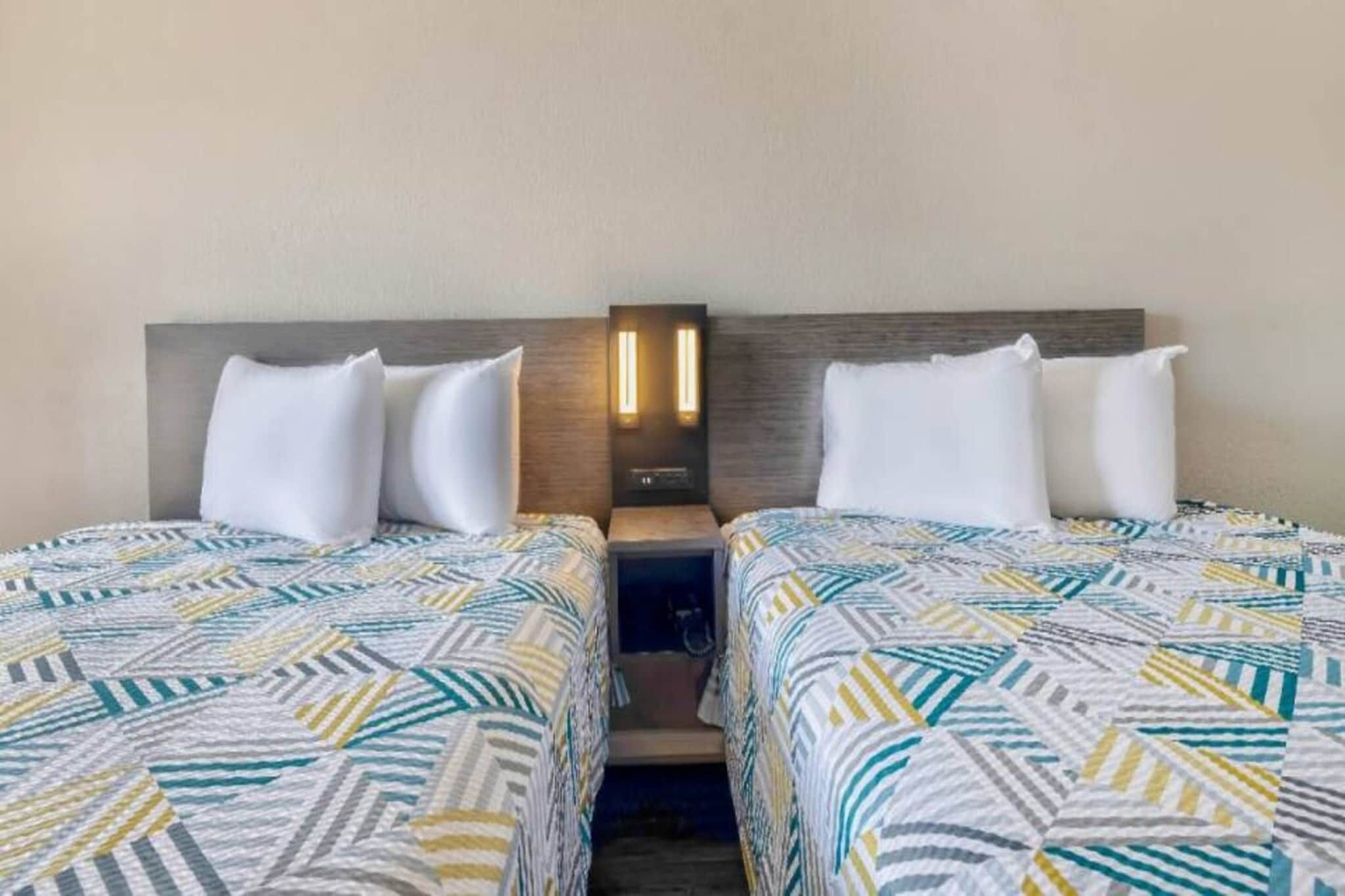 Ein Hotelzimmer mit zwei Betten, jeweils mit einem gemusterten Überwurf, einem Nachttisch mit Lampe sowie einer Wandleuchte.