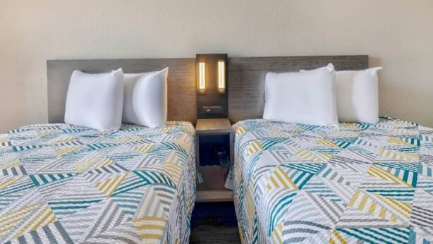 A hotel room with two beds, each with a patterned bedspread, a nightstand with a lamp, and a wall-mounted light fixture. - 2 Queen Beds | Suite, Nsmk, Kitchen (Effingham)