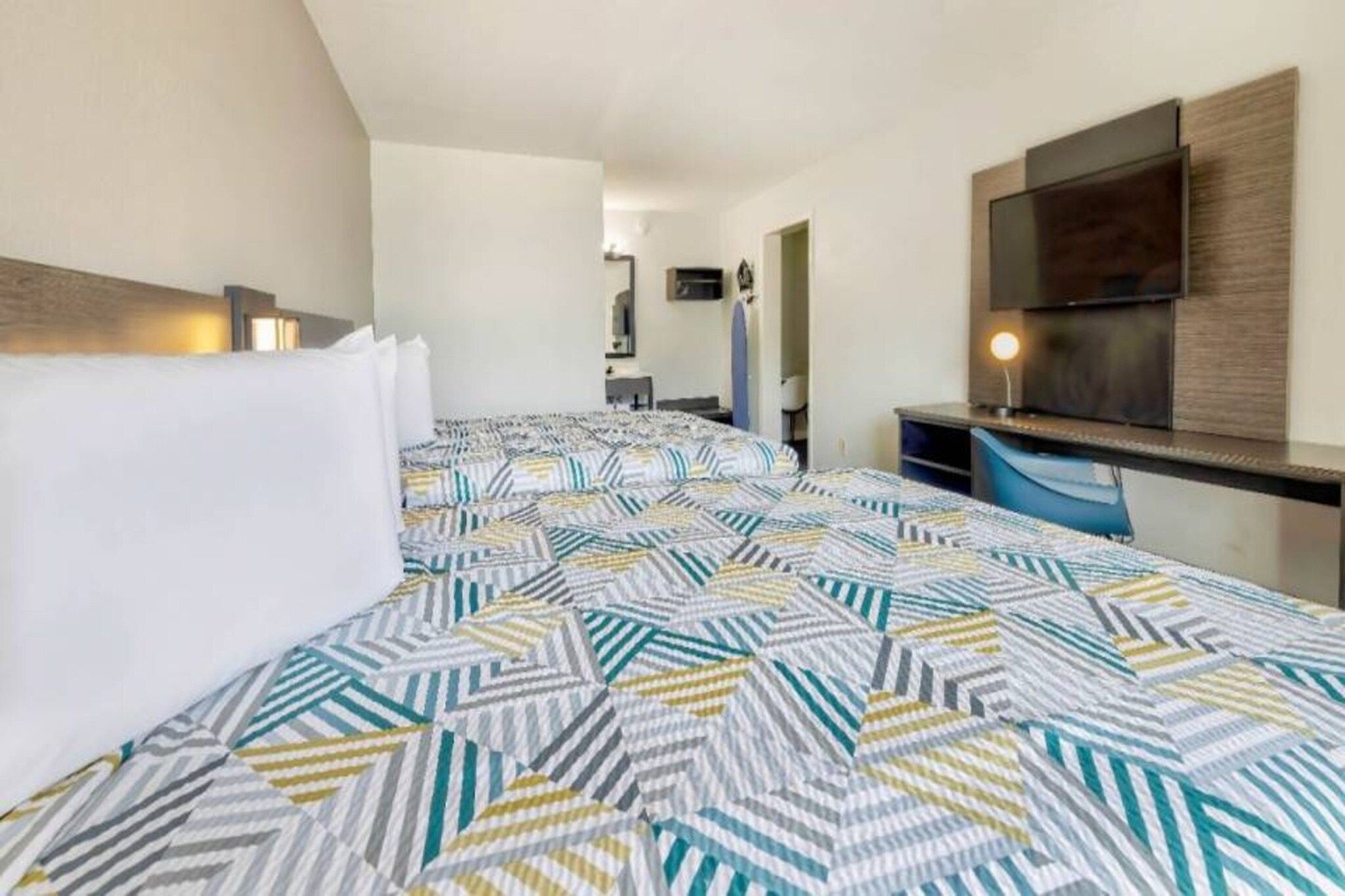Ein Hotelzimmer mit einem gemusterten Bettbezug, einem wandmontierten Flachbildfernseher und einem Schreibtisch mit einer Lampe.