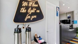A hotel reception area with a neon sign, two coffee dispensers, and a small table with cups and snacks. - 1 King Bed | Non-Smoking (Aransas Pass)