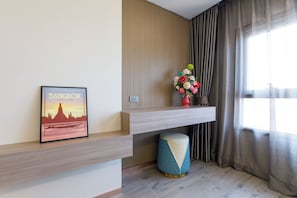 Un interior moderno con un cuadro enmarco de Bangkok, un jarrón decorativo con flores y un taburete redondo azul y blanco.