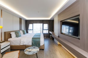 A modern hotel room with a large bed, a flat-screen TV mounted on the wall, and a small round table.