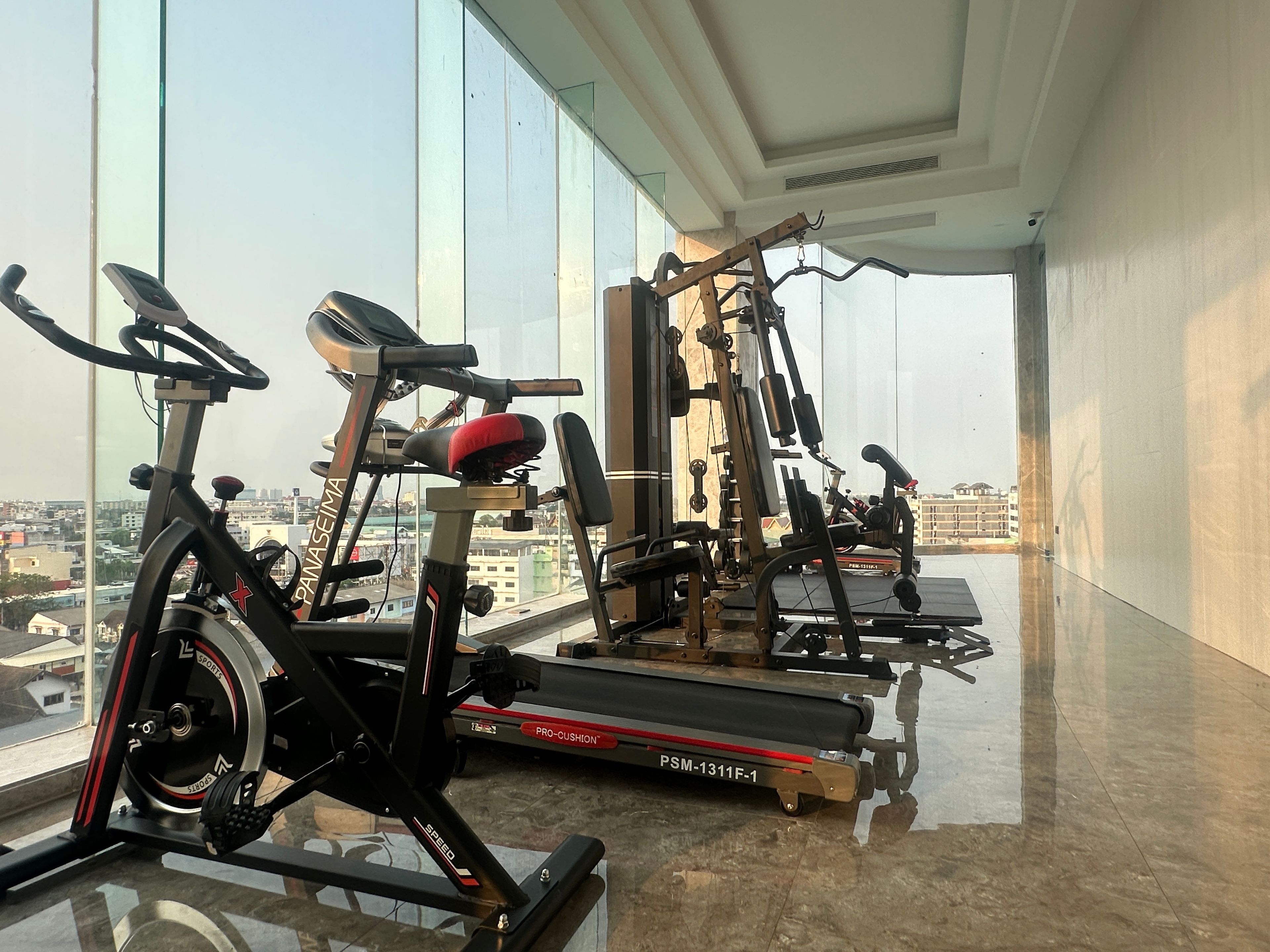 Un gimnasio con equipo de ejercicio, incluyendo cintas de correr y una bicicleta estática, en una sala con ventanas amplias.