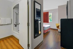 A room with a shower, a bed, a chair, and a refrigerator. - 1 Full Bed | Premium, Micfridge (Orlando FL)