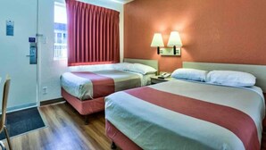 Quarto de hotel com duas camas, janela com cortinas, mesa de cabeceira com luminárias e porta com placa.
