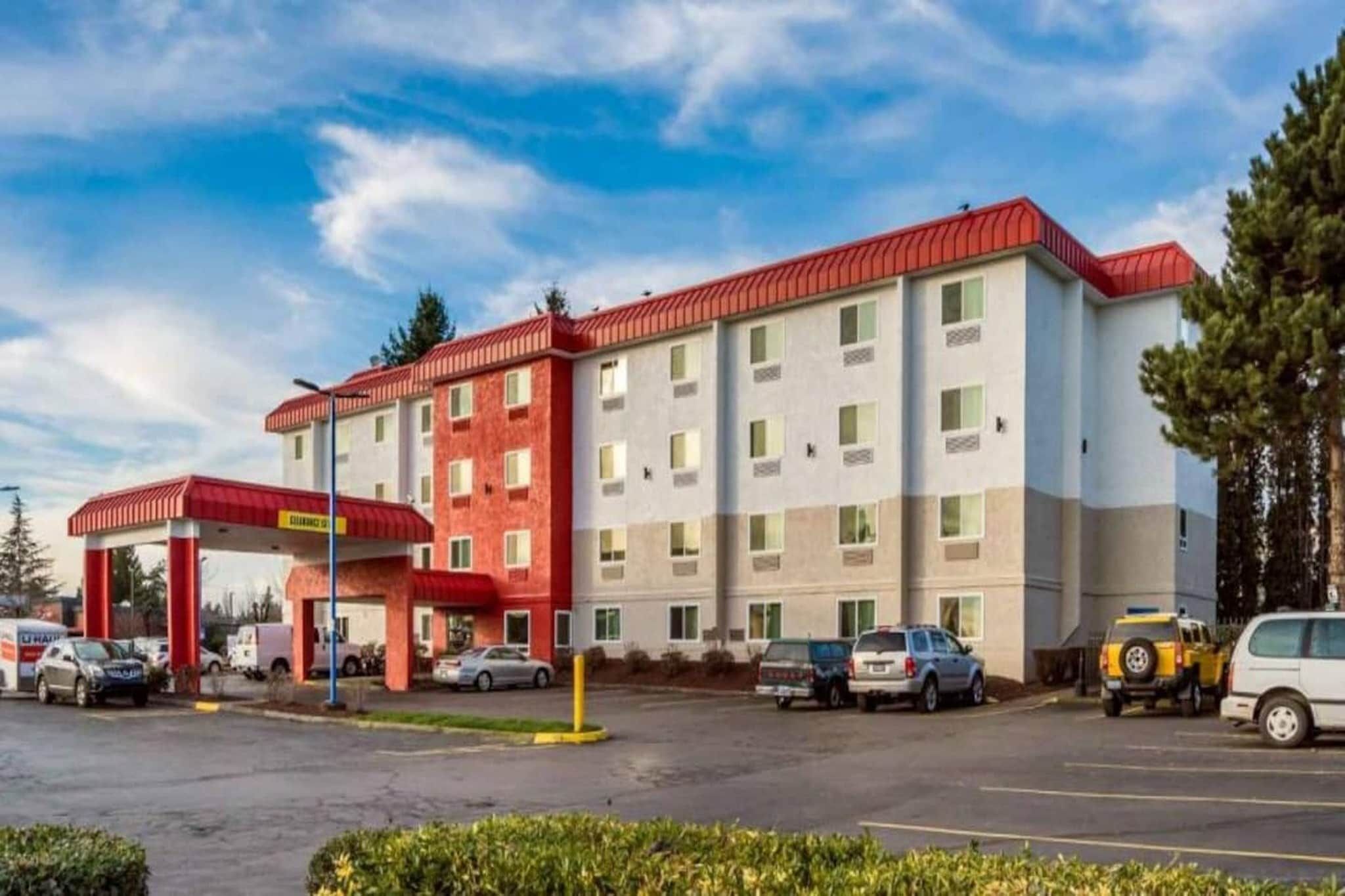 A multi-story hotel with a red and white facade, a gas station with a red canopy, and several parked cars.