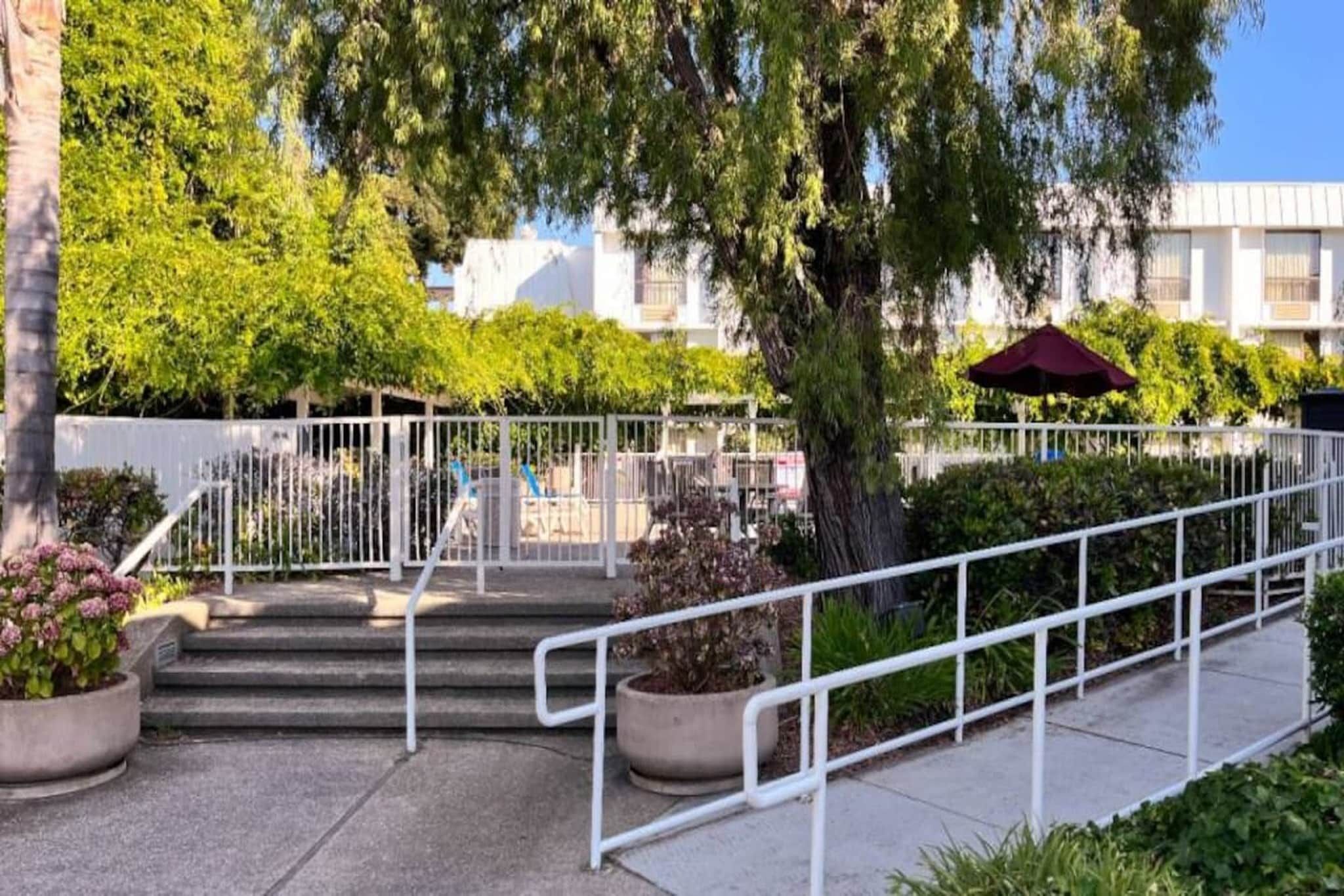 A set of outdoor stairs with metal railings, surrounded by greenery and a building in the background.