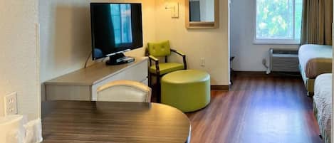 Une chambre d’hôtel avec une télévision, un fauteuil vert, une table ronde et un lit.