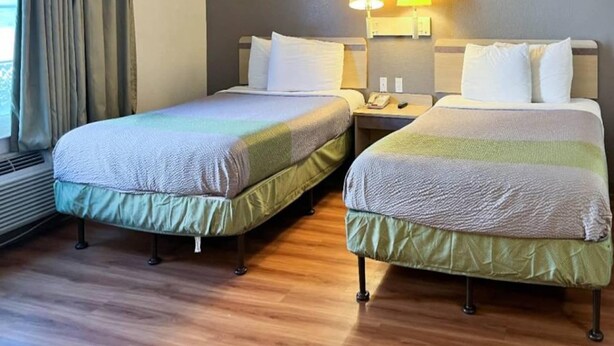 Una habitación de hotel con dos camas individuales, una mesita de noche con lámpara y una ventana con cortinas.