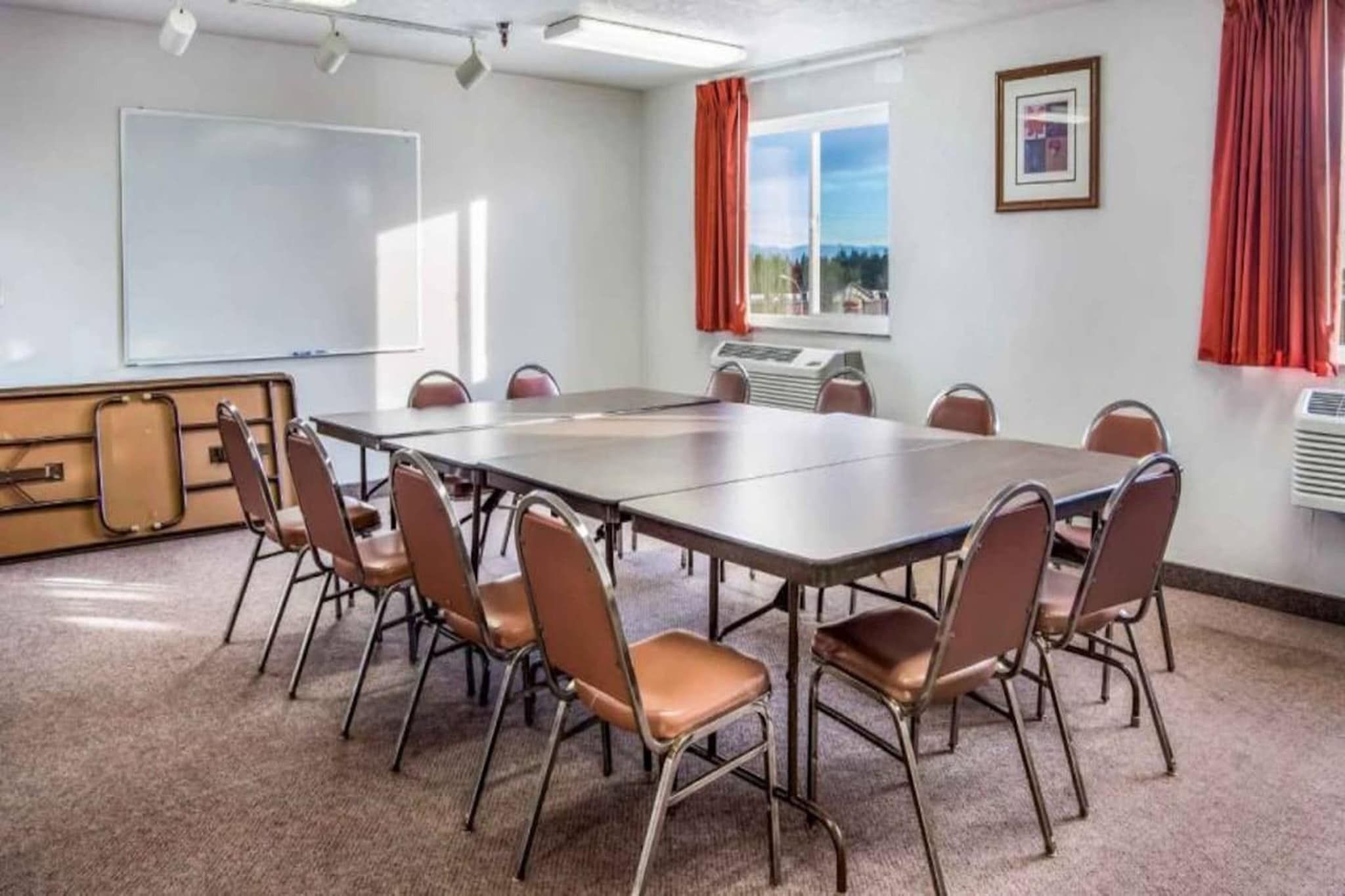A conference room with a large table, chairs, a whiteboard, and a window with curtains.