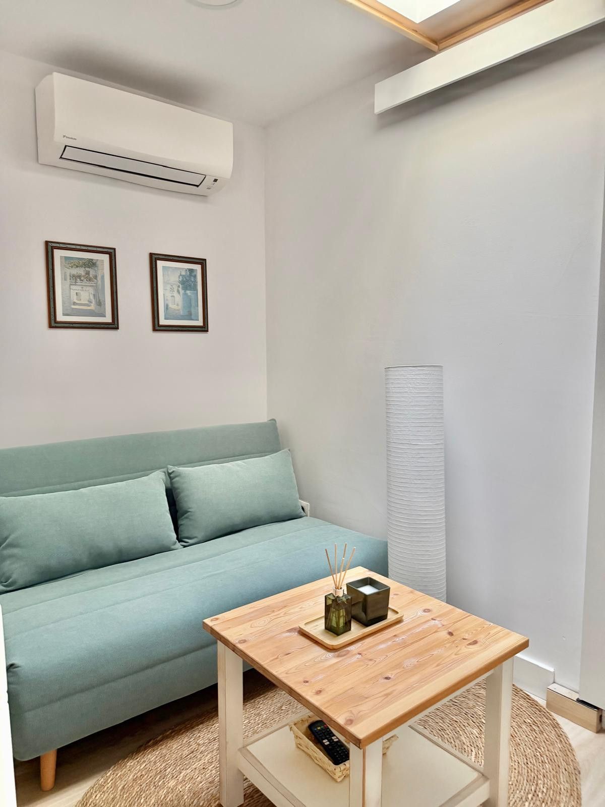 Ein Zimmer mit einem hellblauen Sofa, einem kleinen Holztisch mit einer Vase und Räucherstäbchen sowie zwei gerahmten Bildern an der Wand.