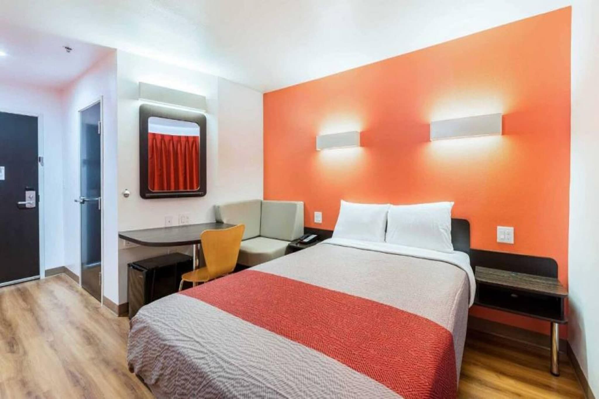 A hotel room with a bed, a desk, a chair, and a nightstand.
