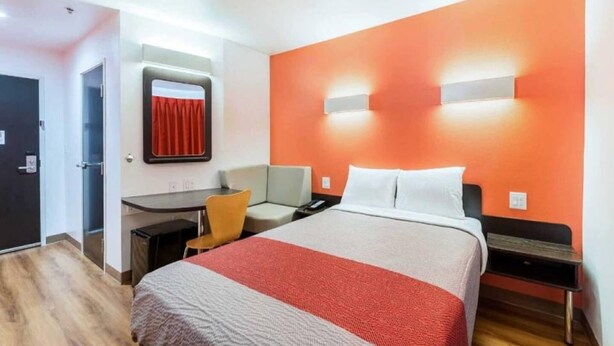 A hotel room with a bed, a desk, a chair, and a nightstand. - 1 Queen Bed|Smk| Fridge (Fort Worth)